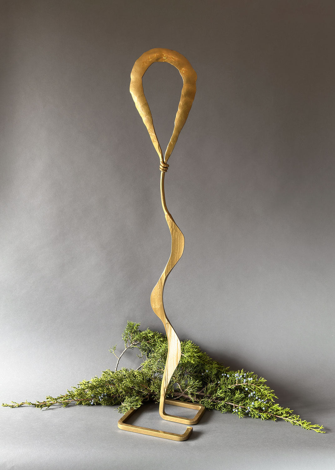Gold metal sculpture with wavy design on a gray background