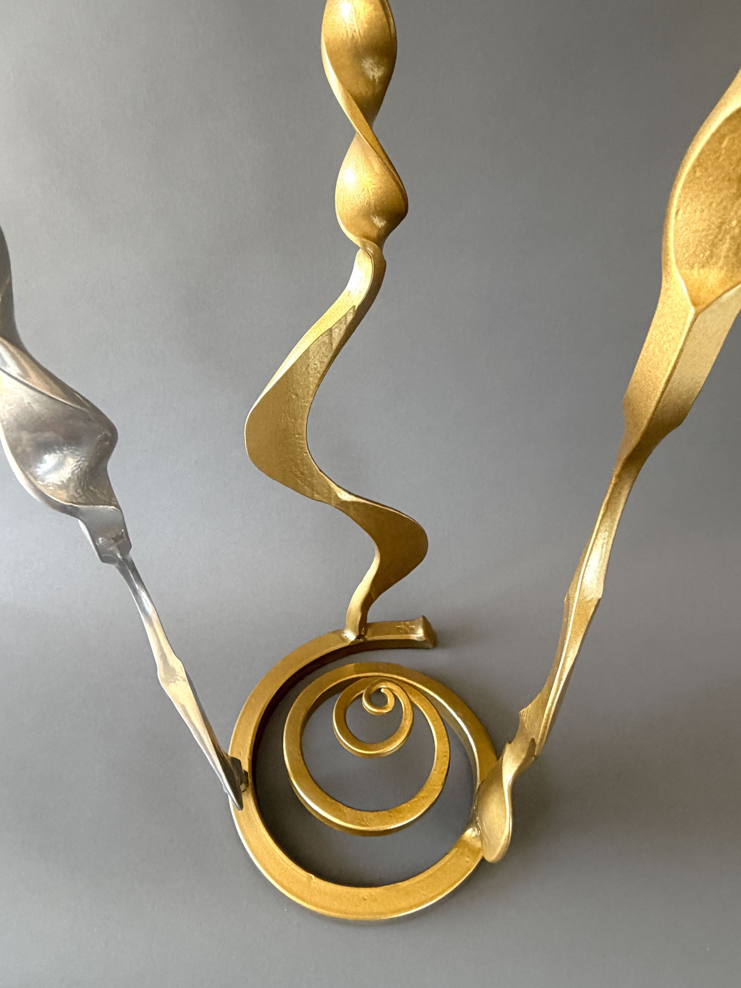 Forged steel Baby Bloom sculpture showing circular freestanding base with hand forged spiral detail and gold metallic finish.
