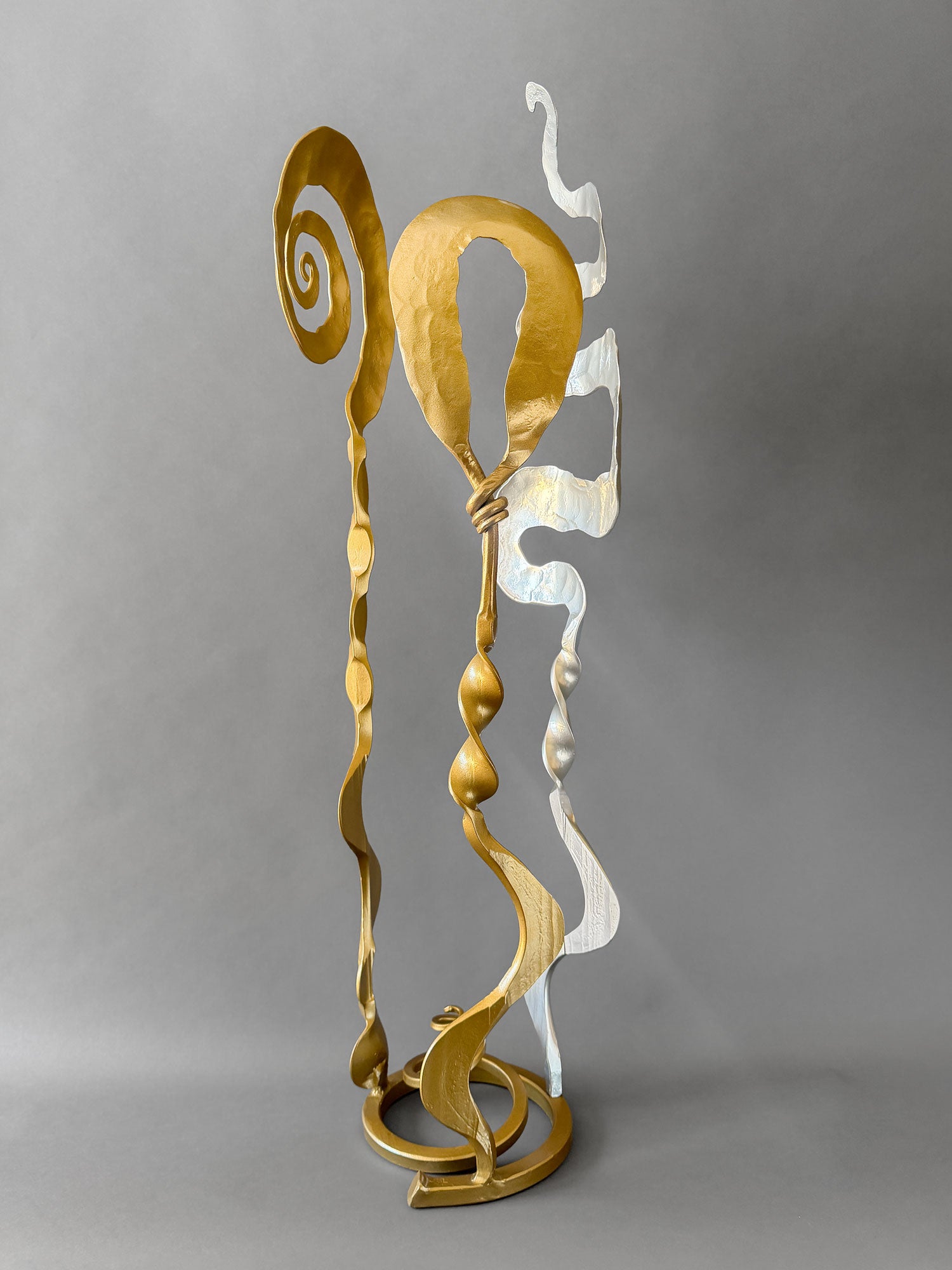 Hand forged Baby Bloom sculpture in metallic gold and chrome finishes featuring abstract spirals and ribbon-like steel forms.