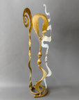 Hand forged Baby Bloom sculpture in metallic gold and chrome finishes featuring abstract spirals and ribbon-like steel forms.