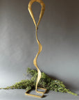Gold metal sculpture with wavy design on a gray background