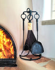 A small rustic fireplace tool set made of hand forged steel, standing next to a kiva fireplace.