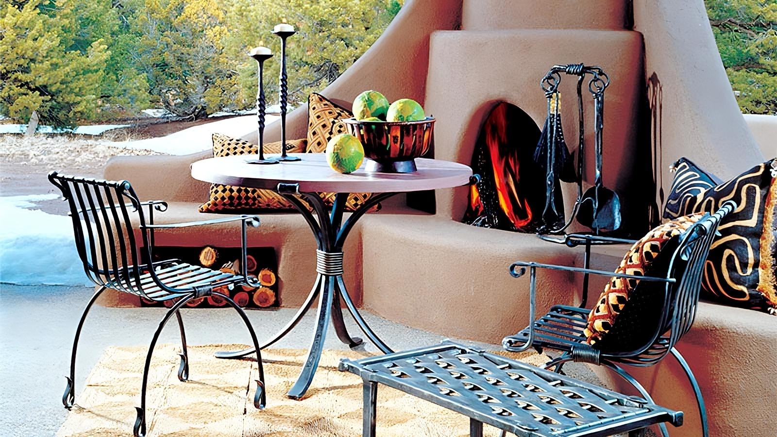 Hand Forged wrought iron patio furniture by an outdoor kiva fireplace. Products are made by New Mexico blacksmith, Christopher Thomson and include wrought iron fireplace tools, wrought iron candlestick holders, iron bench, wrought iron table and chairs.