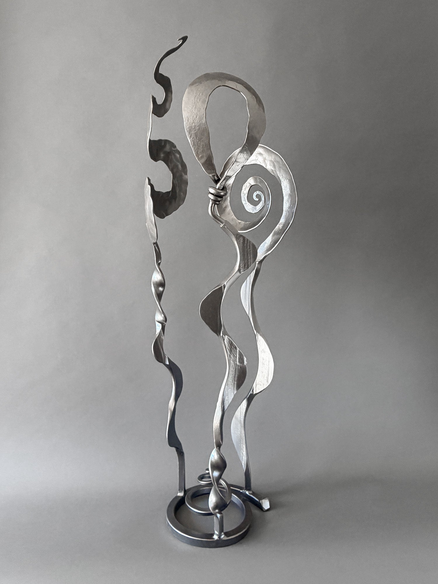 Metallic Baby Bloom steel sculpture combining Meander, Balloon, and Rose forms with spiraling and flowing hand-forged elements on a circular base.