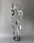 Metallic Baby Bloom steel sculpture combining Meander, Balloon, and Rose forms with spiraling and flowing hand-forged elements on a circular base.