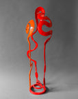 Orange and red hand forged steel Baby Bloom sculpture, front view, with large orange Rose spiral, red Meander and red Loop forms on circular base, 33 inches tall