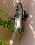 Hand forged wall lantern with hand blown glass mounted on an adobe exterior wall, surrounded by climbing greenery