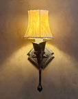 A small wrought iron calla lily wall sconce with a sheepskin shade mounted to an adobe wall with a diamond shaped backplate.