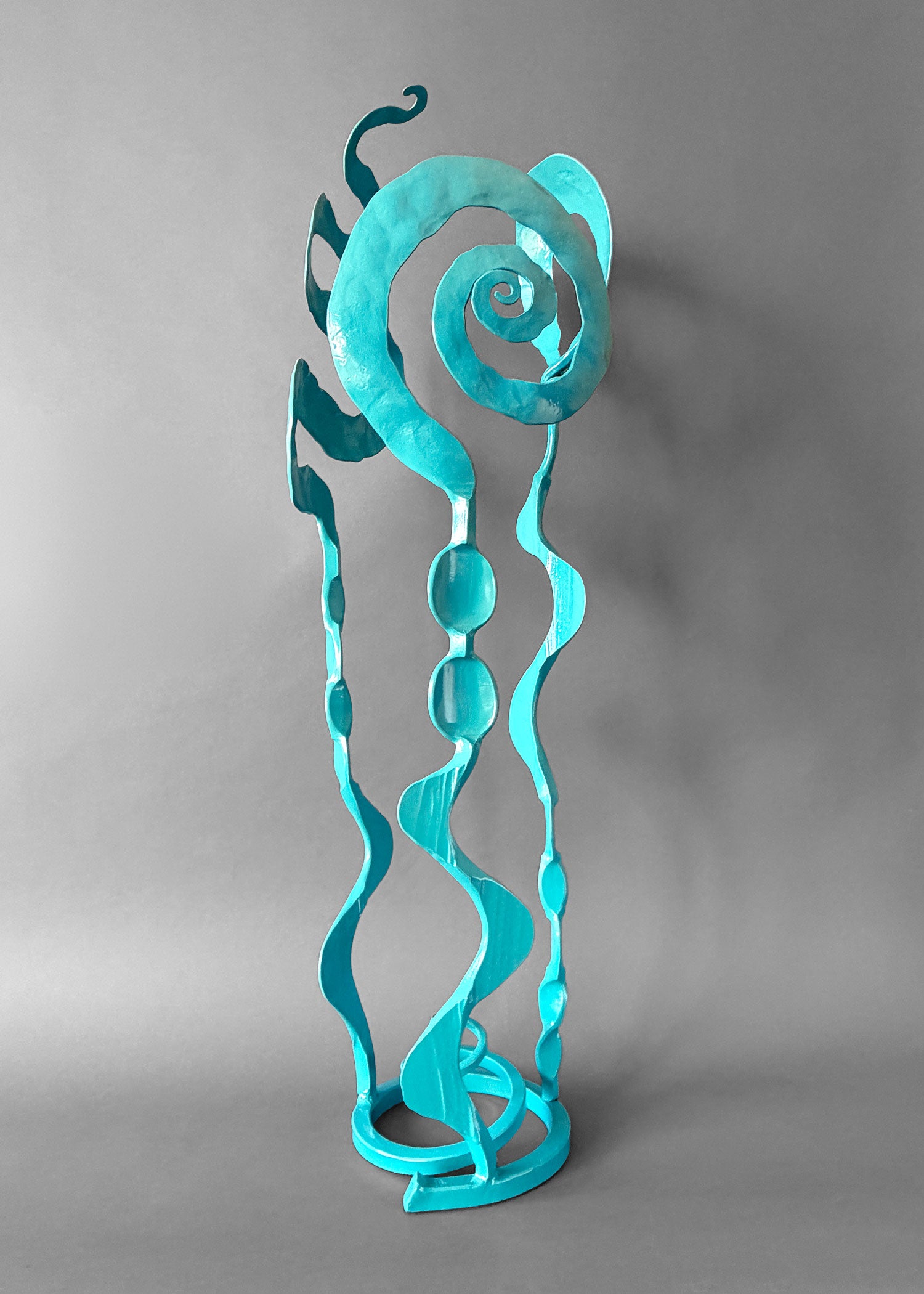 Turquoise metal sculpture with swirling design on a gray background