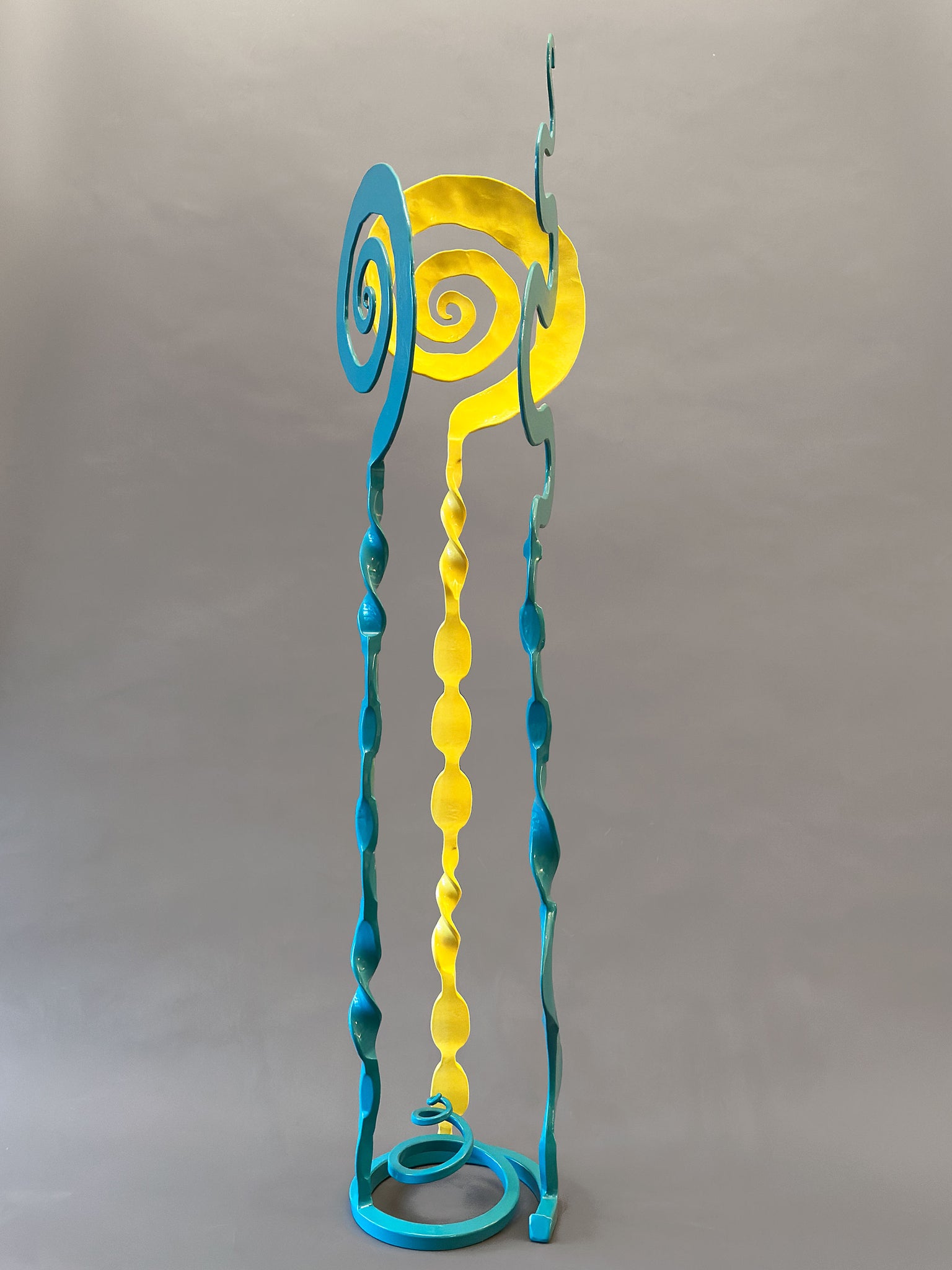 Turquoise and Yellow small sculpture that has two turquoise elements and one yellow element. All three elements are welded onto a spiral turquoise base,