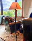 A Wrought Iron Vine Lamp in a Southwestern style living room with a leather chair, couch, kiva fireplace and view of trees outside a window.
