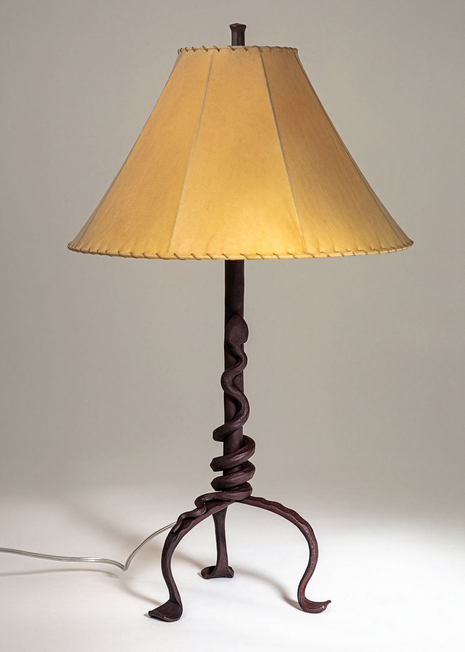 Western Rattlesnake wrought iron lamp with a forged steel rattlesnake wrapped tightly around the base of the light fixture's stem. Shown with a handmade sheepskin shade.