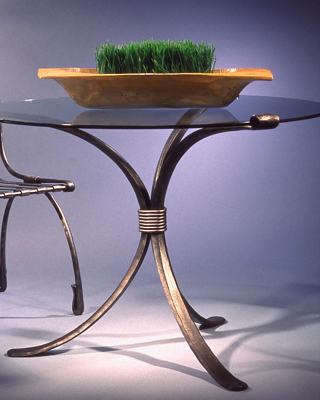 Close-up of a wrought iron dining table base, three hand forged legs bound by a wrapped collar and ending in flat paddle feet