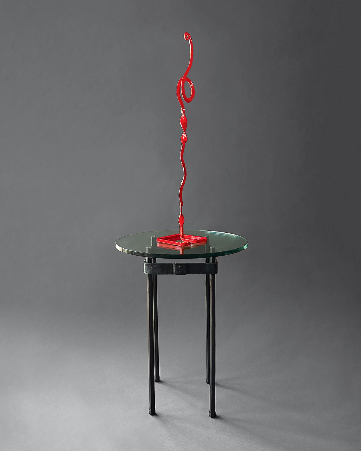 Wrought iron pedestal table with a round glass top displaying a red hand forged steel sculpture