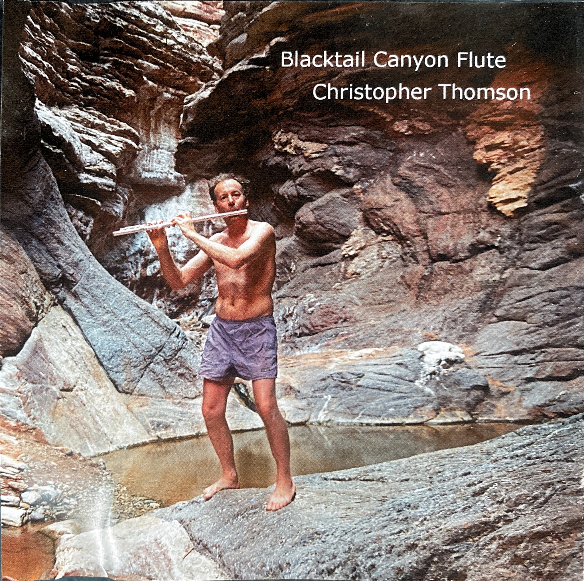Album cover with a man wearing swimming trunks playing flute in a cave. Reads "Blacktail Canyon Flute" and "Christopher Thomson".