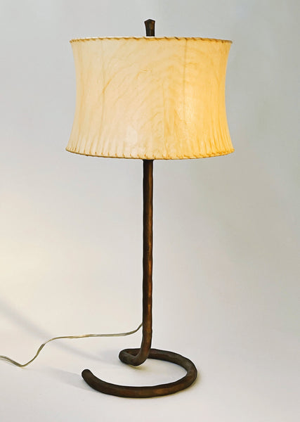 Rust finished wrought iron table lamp with an open half circle base and a contemporary drum sheepskin shade. 