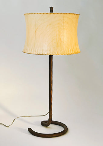 Rust finished wrought iron table lamp with an open half circle base and a contemporary drum sheepskin shade. 