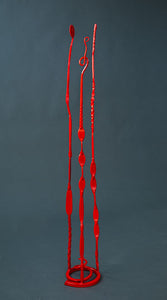 A red hand forged sculpture that has three long pieces emerging from the spiral base.