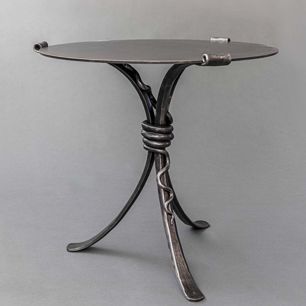 A three legged hand forged wrought iron table featuring a hand forged rattlesnake wrapped around the center of the table legs.