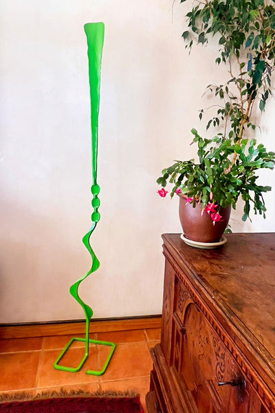 Indoor setting showing Green Beads Feather Free Standing Single Bloom sculpture next to indoor plants.